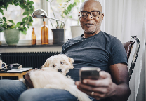 Man met hond op schoot kijkt op mobiel