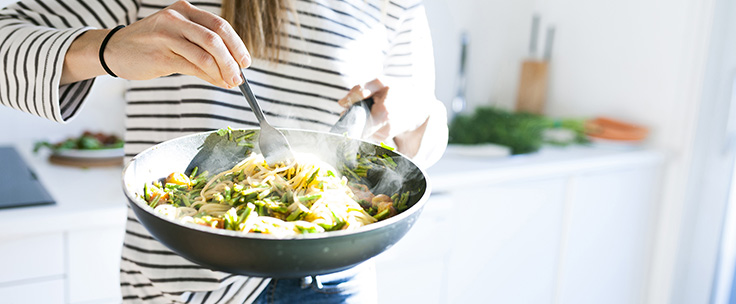 Vrouw in keuken schept gerecht uit pan