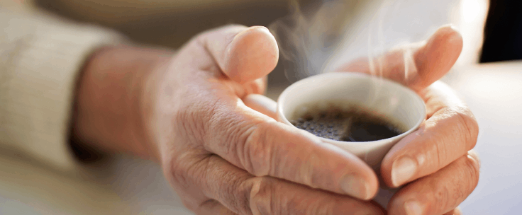 Handen om een warme kop koffie heen