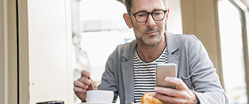 Man kijkt op zijn mobiel met een kop koffie erbij