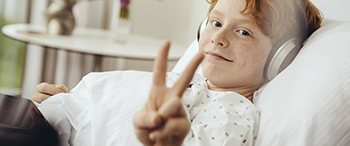 Jongen in bed met hoofdtelefoon op maakt steekt 2 vingers omhoog