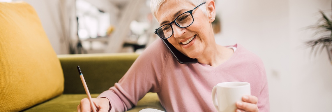 Lachende vrouw belt en schrijft met een koffie erbij